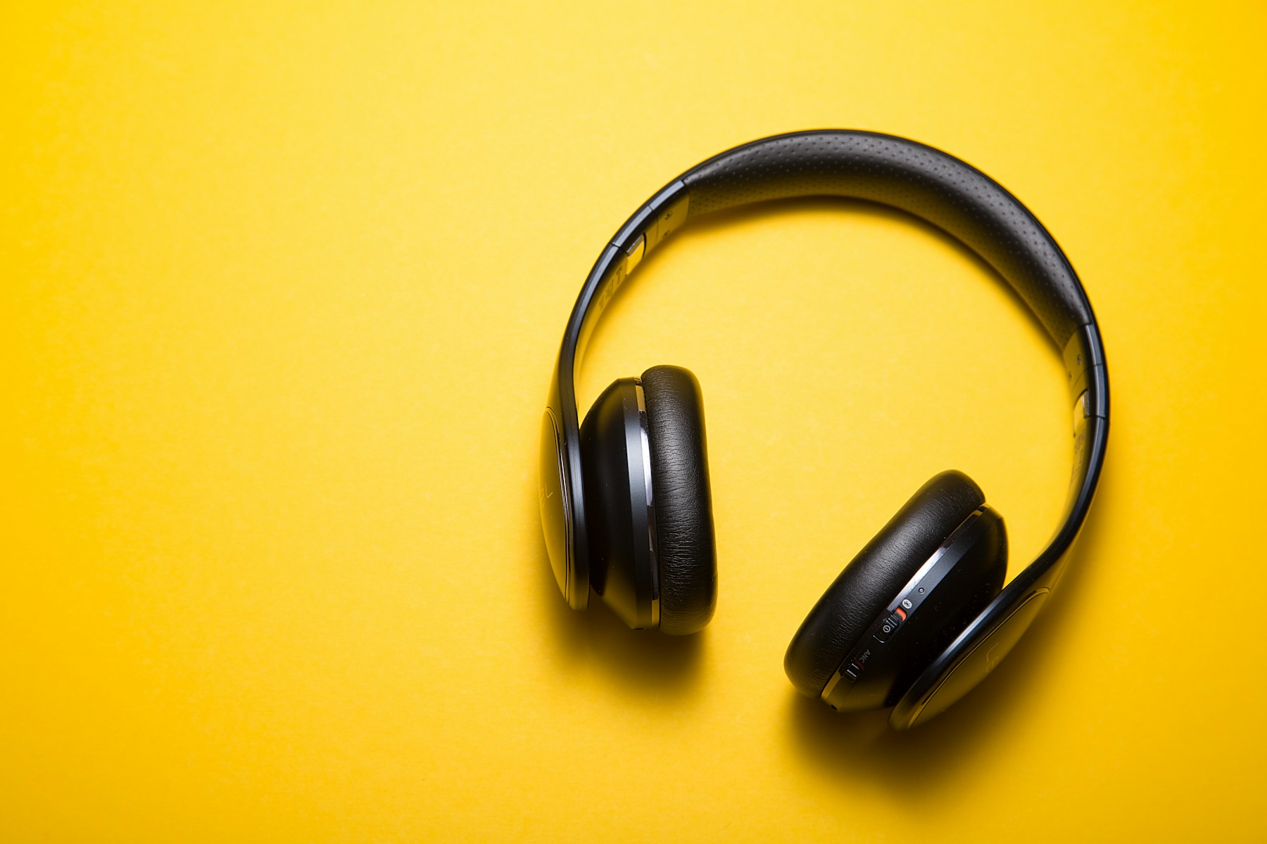 Black wireless headphones on a vivid yellow surface